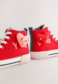 Baskets montantes rouges avec lacets blancs, semelles blanches, patchs cœur souriant et textes « YOU » et « LOVE » sur les talons.