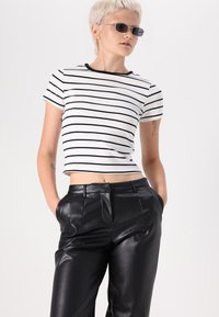 T-shirt branca cortada com riscas horizontais pretas, combinada com calças de couro pretas de cintura alta, com bolsos laterais e uma textura suave.