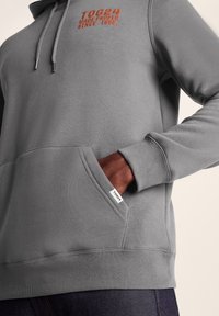 Gray hoodie made from soft cotton blend, featuring a front pocket, drawstring hood, and orange logo text. Ribbed cuffs and hem.