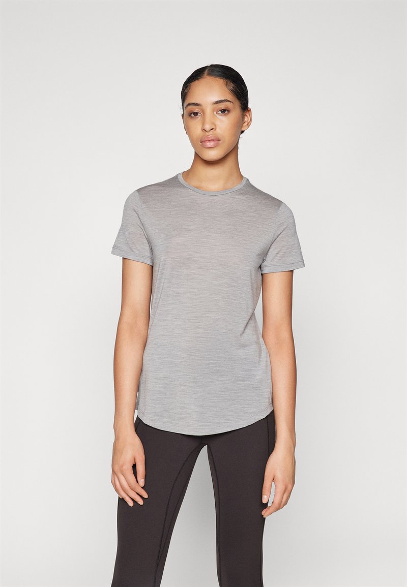 T-shirt cinza de manga curta com decote redondo e uma bainha ligeiramente curva, feita de um tecido suave e leve, combinada com leggings pretas.