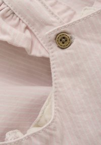 Ljusrosa tyg med subtila vita ränder, med en volangkant och en rund, beige knapp med dekorativa sömmar.