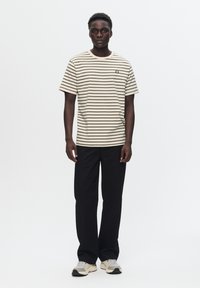 Tricou cu dungi bej și maro, cu guler rotund, asortat cu pantaloni negri și adidași gri deschis. Design simplu, cu branding subtil.