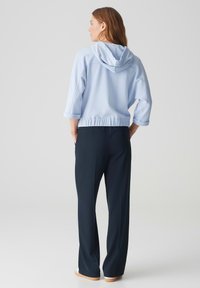 Felpa blu chiaro con cappuccio regolabile, design corto e vita elasticizzata, abbinata a pantaloni blu navy e calzature di colore chiaro.