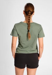 T-shirt in cotone verde oliva con collo rotondo e maniche corte, abbinato a pantaloni corti neri. Tessuto liscio, vestibilità comoda e senza motivi visibili.