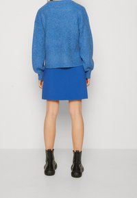 Blue knit sweater with a cropped design, paired with a blue mini skirt. Black ankle boots feature a zip closure and rounded toe.