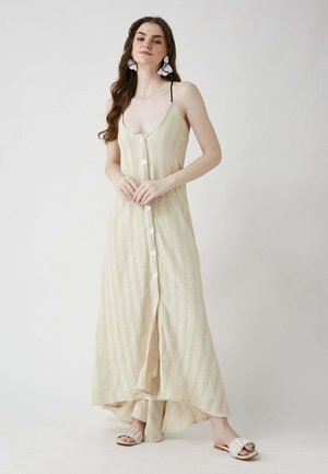 Strick-Maxikleid in hellbeige mit vertikalen Streifen, mit einer Knopfleiste und verstellbaren Trägern. Kombiniert mit schneeweißen Riemchensandalen.
