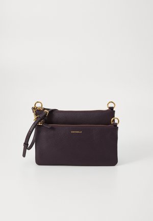 Pochette en cuir violet foncé avec des fermetures éclair dorées, des anneaux et un petit nom de marque "Coccinelle" au centre avant.