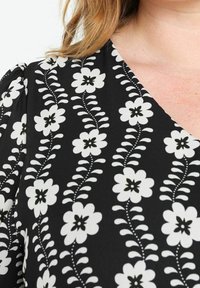 Tissu noir avec un motif floral blanc aux centres noirs. Comprend des manches amples et un décolleté en V.