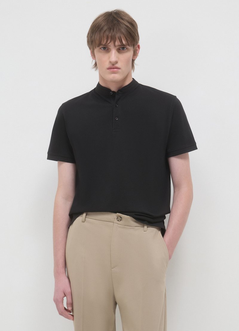 Polo nera con collo alto e abbottonatura a tre bottoni. Indossata con pantaloni beige chiaro, tessuto liscio e vestibilità sartoriale.