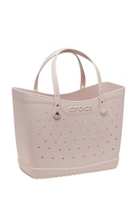 Różowa torba tote z gumy z perforowanym wzorem, dwoma solidnymi uchwytami i teksturowanym dnem. Na przodzie znajduje się logo "CROCS".
