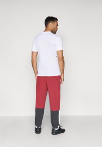 Λευκό αθλητικό μπλουζάκι κοντομάνικο σε συνδυασμό με σορτσάκι τρεξίματος με κόκκινες και γκρίζες ρίγες. Μαύρα αθλητικά παπούτσια ολοκληρώνουν το σύνολο, τονίζοντας τον αθλητικό σχεδιασμό.