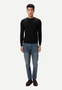 Pull en maille noire, jean denim bleu clair, chaussures marron. Le pull présente un col rond et une coupe slim. Le jean est droit avec une légère usure.