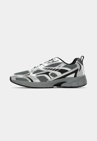 Šedá a černá sportovní běžecká bota s síťovaným svrškem, šněrováním, silnou podrážkou a poutkem na patě, na bílém pozadí.