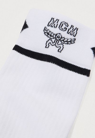 Chaussette blanche avec des rayures noires et un graphique noir d'une tête de mort ailée portant une couronne, avec l'acronyme "MGM" au-dessus.