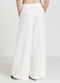 Pantaloni larghi bianchi realizzati in un tessuto morbido, dotati di due tasche posteriori con cuciture discrete e una vita senza cuciture.