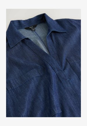 Cămașă din denim albastru închis cu guler, deschidere în formă de V și buzunare vizibile în față pe piept, așezată plat pe o suprafață deschisă la culoare.