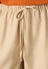 Pantalons beiges à cordon de serrage en tissu texturé. Dotés d'une taille élastique et de liens, avec des détails de couture raffinés.