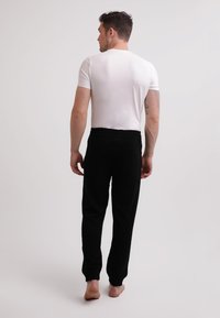 Czarne dresy z bawełny o luźnym kroju, z elastycznym paskiem w talii i bocznymi kieszeniami, pokazane od tyłu na modelce boso.