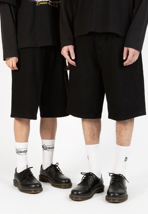 Shorts en denim noir à coupe ample, chaussures noires à lacets et chaussettes blanches avec du texte noir. Design simple et dépouillé.