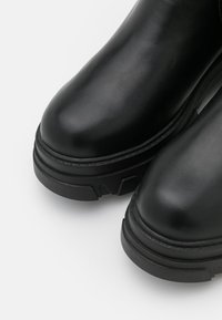 Botas negras hasta el tobillo hechas de cuero suave con punteras redondeadas, suelas de goma gruesas y acentos texturizados en los laterales.