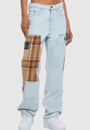 Light blue denim pants with brown plaid patch accents on the thighs, featuring a relaxed fit and side pockets. White sneakers complete the look.
