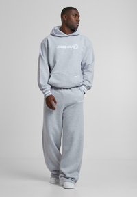 Gray sweatshirt and matching sweatpants made of soft fabric. Features a hood, ribbed cuffs, and white logo on the front and leg.