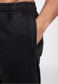 Zwarte sweatpants met een elastische tailleband, zijzak en een gladde katoenen textuur, weergegeven van de taille tot de bovenkant van de dij.