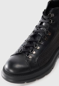 Stivale alla caviglia in pelle nera con tessuto testurizzato, accessori in metallo argentato e lacci a contrasto. Suola robusta con design della punta rotonda.
