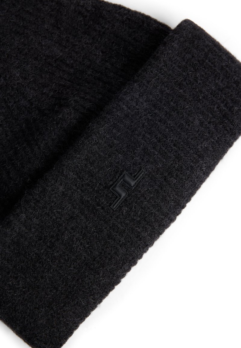 Berretto in maglia nera realizzato in lana texture, dotato di risvolto e un piccolo patch logo nero sul lato.
