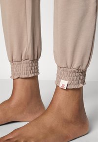 Pantaloni jogger beige chiaro con polsini arricciati e una piccola etichetta del marchio sull'orlo. Tessuto liscio e elasticizzato con una vestibilità rilassata.