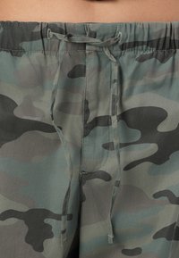 Shorts camouflage avec une ceinture à cordon, présentant un mélange de verts et de gris, une texture lisse, et des poches latérales.