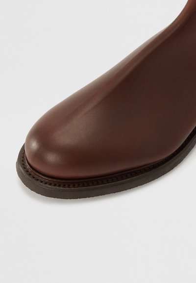 Botte de cheville en cuir marron avec un bout arrondi, finition lisse et semelle en caoutchouc marron contrastante. Détails cousus autour du bord de la semelle.