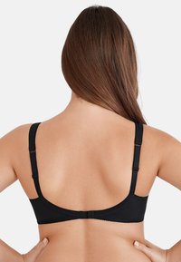 Reggiseno nero con spalline regolabili, texture morbida e finitura liscia. Presenta un design semplice e un bordo ondulato lungo l'elastico.