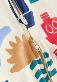 Vêtement en coton zippé présentant des motifs abstraits colorés en rouge, bleu, beige et vert menthe sur un fond crème.