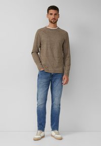 Brauntexturiertes Langarmhemd mit einem weißen Rundhalsausschnitt, kombiniert mit hellblauen geraden Jeans und weißen Sneakers mit beigen Akzenten.