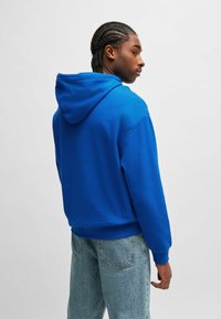 Blue hooded sweatshirt featuring a relaxed fit, ribbed cuffs and hem, with a soft texture. Paired with light blue denim pants.