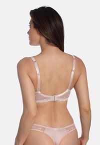 Hellrosa Spitzen-BH mit Punkten, verstellbaren Trägern und Hakenverschluss. Glatte Textur mit gewellten Kanten.