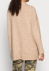 Beige oversized Pullover mit strukturiertem Strick, gerippten Bündchen und Saum. Kombiniert mit grünen Cargohosen im Camouflage-Muster.