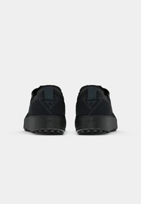 Nike apavi ar melnu zamša augšdaļu, plakanu papēdi un biezu gumijas zoli ar strukturētu saķeres rakstu. Aizmugures skats parāda pastiprinātu papēža cilpu.