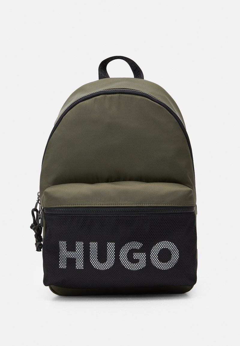 Sac à dos en nylon vert avec un sommet arrondi, poche en mesh noir et logo "HUGO" blanc. Comprend une fermeture zippée et une poignée supérieure.