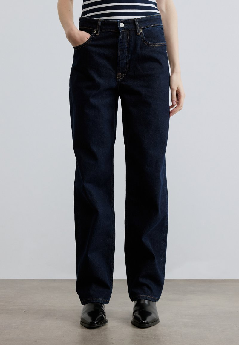 Σκούρο μπλε τζην με ίσια γραμμή, μπροστινές τσέπες και χρυσή ραφή. Συνδυασμένα με ριγέ τοπ και μαύρα παπούτσια.