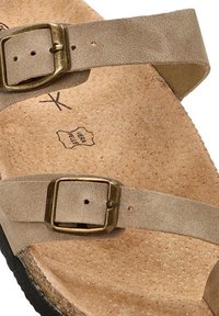 Sandalia de cuero beige con dos correas ajustables y hebillas de latón. La plantilla de corcho texturizado y la suela de goma oscura proporcionan contraste.