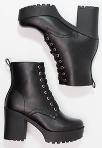 Botas negras hasta el tobillo con un tacón grueso, cordones en la parte delantera y suela de goma texturizada. Hechas de cuero sintético suave con una etiqueta en la parte trasera.