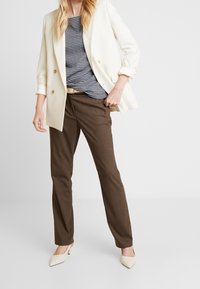 Ivoriefärgad kavaj över en mönstrad blå topp, kombinerad med bruna byxor och krämfärgade spetsiga klackar. Slim fit med knappdetaljer på kavajen.