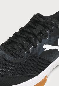 Κοντινό πλάνο μαύρου αθλητικού παπουτσιού Puma με υφασμάτινο δίχτυ, μαύρα κορδόνια, λευκή ενδιάμεση σόλα και χαρακτηριστικό λευκό λογότυπο Puma στο πλάι.