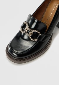 Mocassins en cuir noir avec une semelle épaisse, ornés d'une chaîne en métal argenté sur le dessus. Fini lisse et design à bout rond.