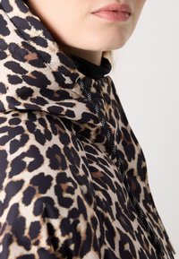Chaqueta con capucha de estampado de leopardo, fabricada en tejido ligero, con un patrón negro y beige, que incluye cordones negros y un diseño de cuello alto.