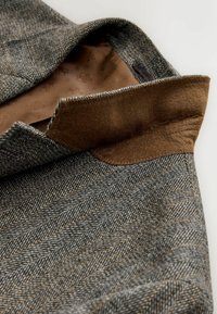 Gray houndstooth fabric with brown accents, showcasing a smooth inner lining and clean stitching along the collar and lapel edges.