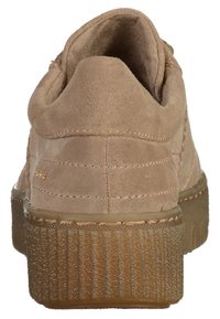 Beige Wildlederschuh mit einer strukturierten Gummisohle, die Rückansicht zeigt eine Nahtdetail und eine erhöhte Ferse, mit subtiler Prägung in Gold.