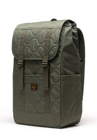 Grüner gesteppter Rucksack mit Klappe, ausgestattet mit zwei vorderen Riemen, einem Logo-Patch und einer seitlichen Netztasche. Glatte Stoffoberfläche.